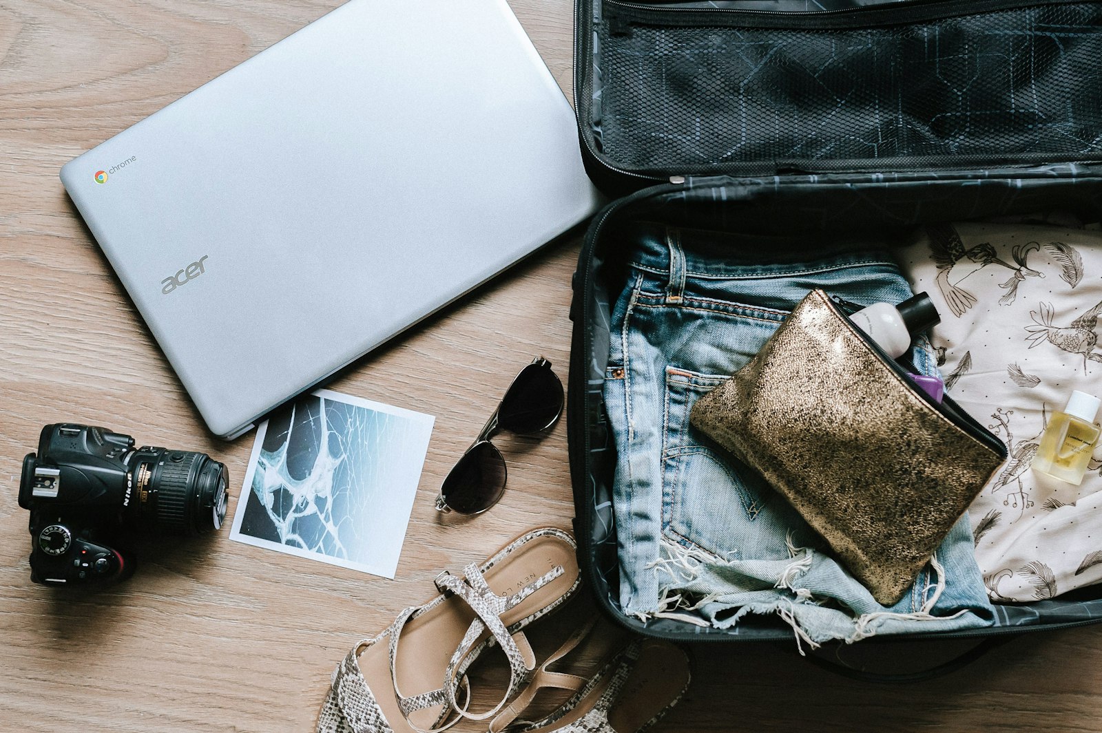 Open suitcase with holiday clothes, camera, sunglasses and laptop