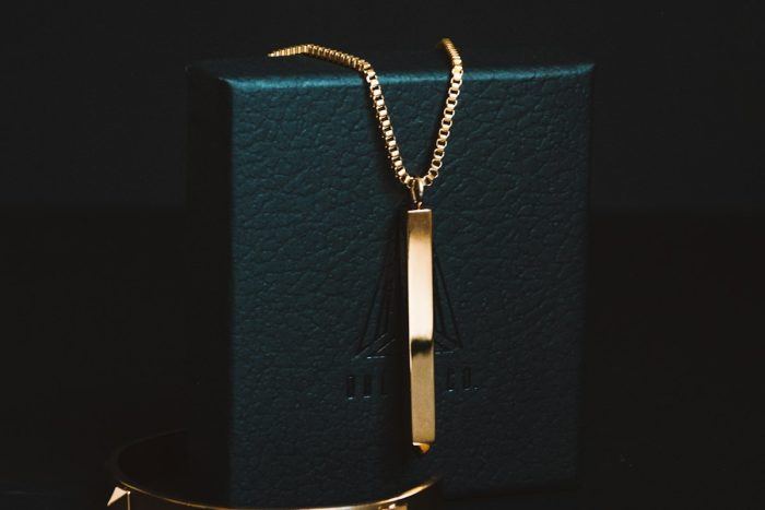 Gold-coloured pendant necklace displayed against a dark jewellery box