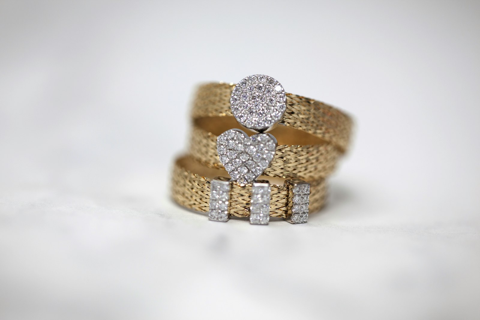 Three gold-coloured rings with sparkling decorative settings on a pale background
