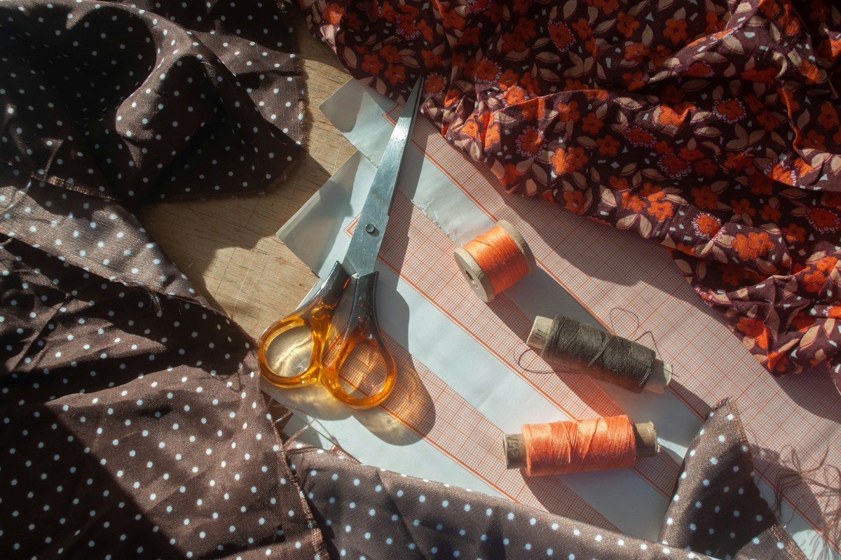 Scissors and orange and brown thread spools on paper patterns surrounded by floral and spotted fabric