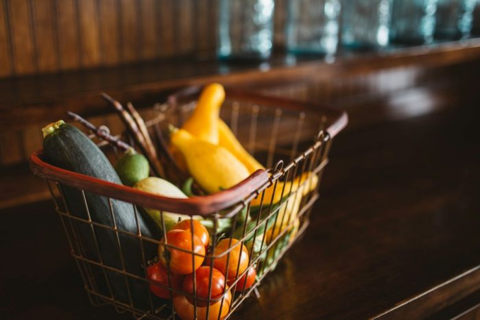 Tomatoes, courgettes and yellow squash in a wire basket on a wooden counter