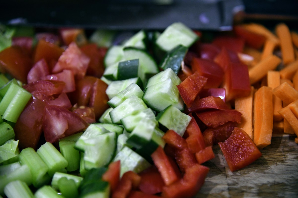 Chopped cucumber, celery, tomatoes, red pepper and carrots arranged on a wooden board