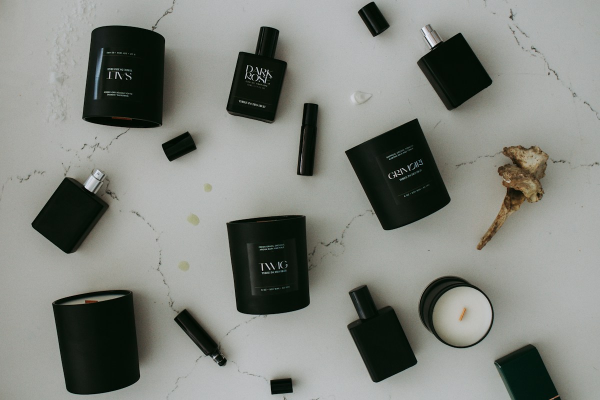 Black perfume bottles, slim atomisers and scented candles arranged on a pale stone surface