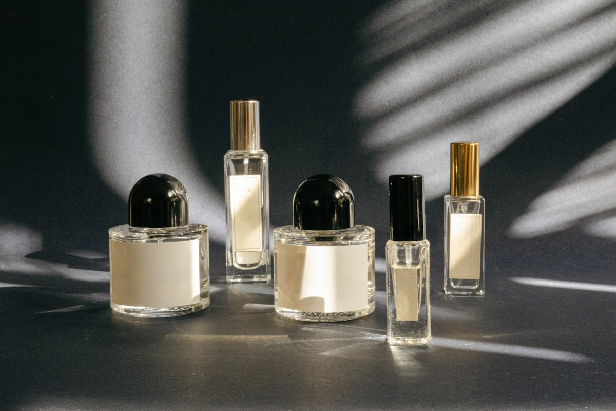 Five clear perfume bottles of different shapes on a grey surface in diagonal sunlight