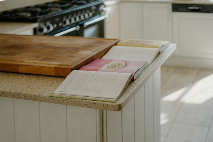 Open cookbooks beside a wooden chopping board on a kitchen island