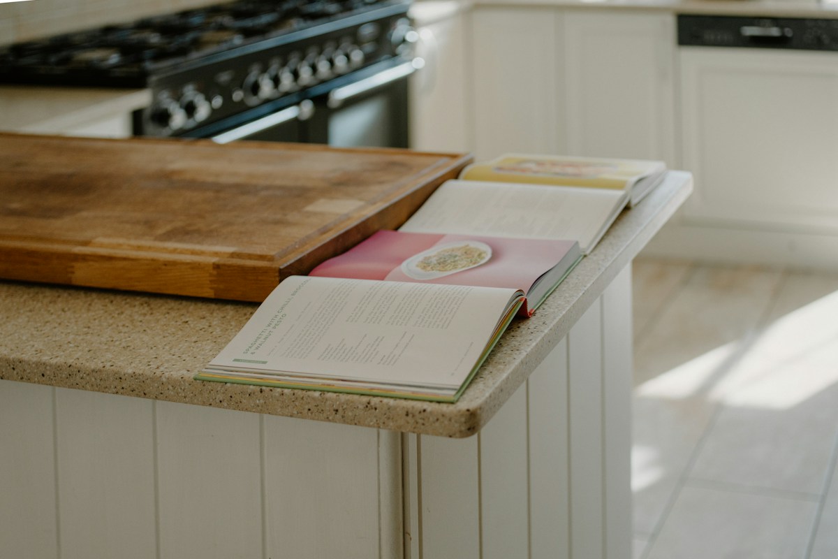Open cookbooks beside a wooden chopping board on a kitchen island