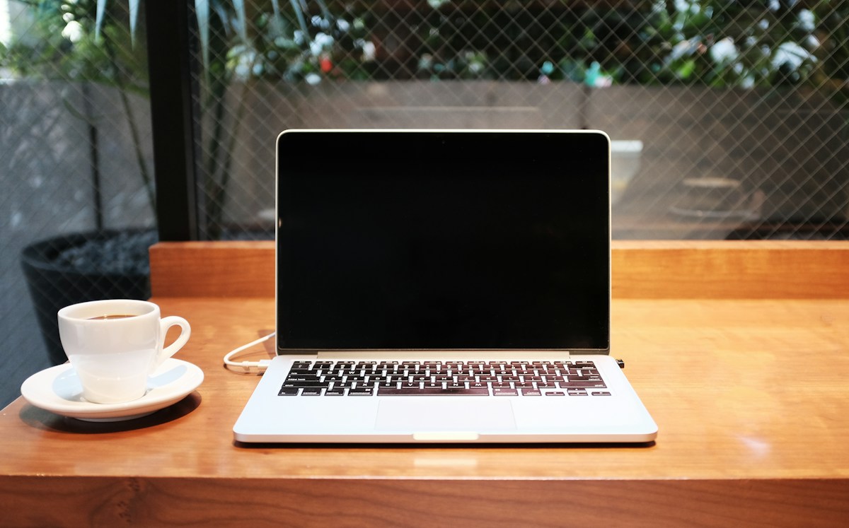 Open silver laptop beside a white coffee cup on a wooden table