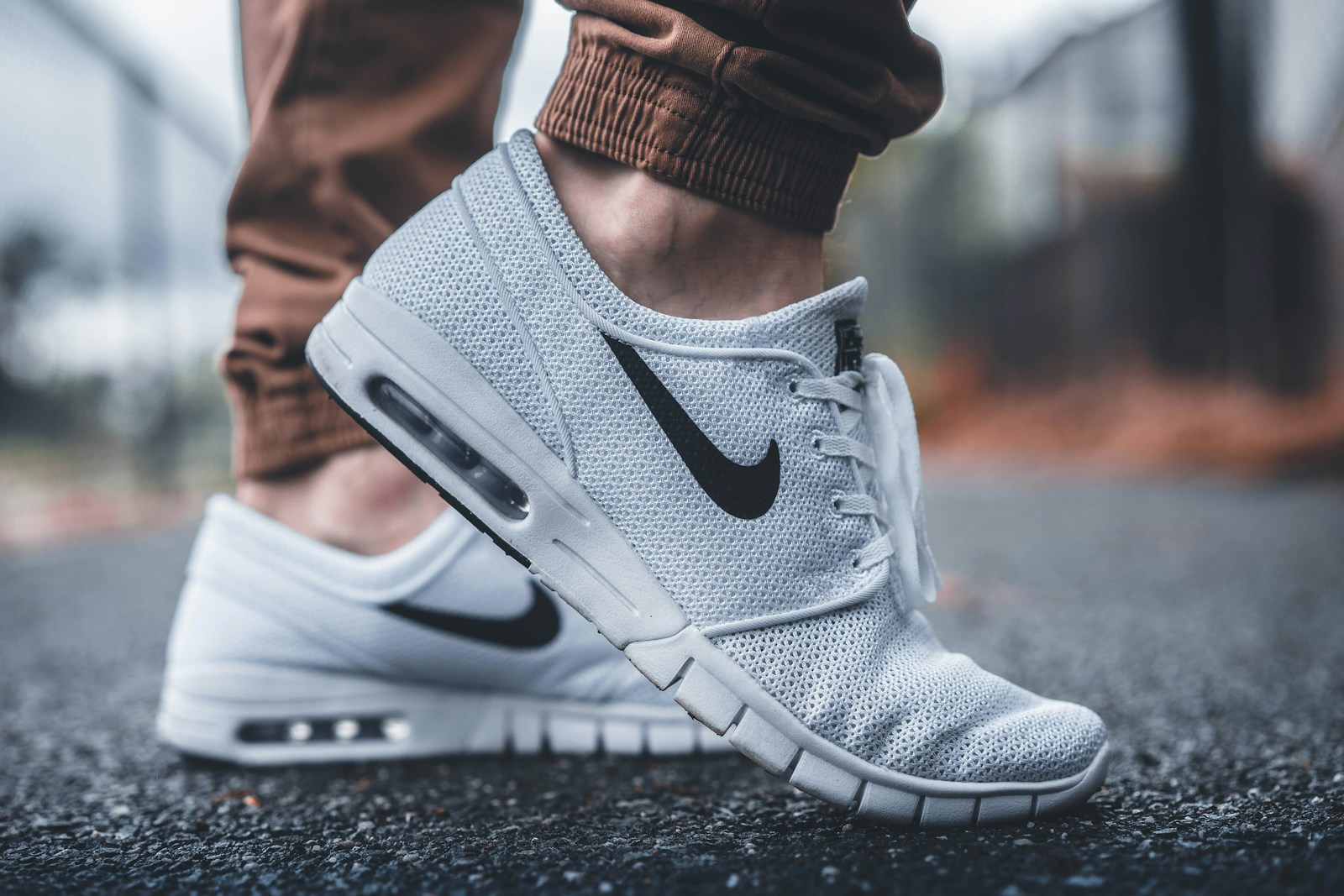 Close-up of light grey Nike trainers with black swooshes on a paved surface